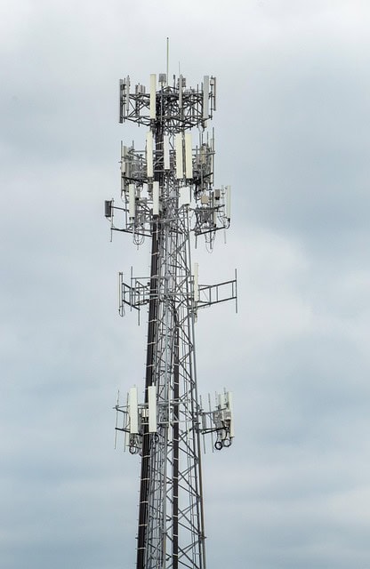 A tall communication tower with multiple antenna arrays stands against a cloudy sky.