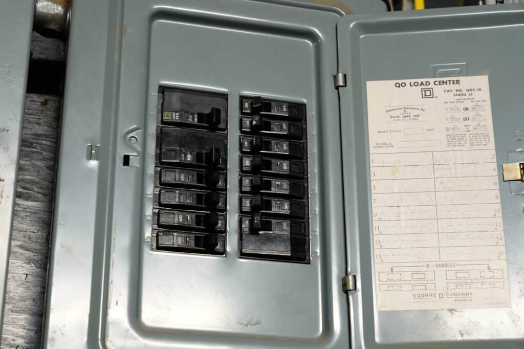 An open electrical breaker panel with multiple switches and a load center diagram attached to the inside of the door.
