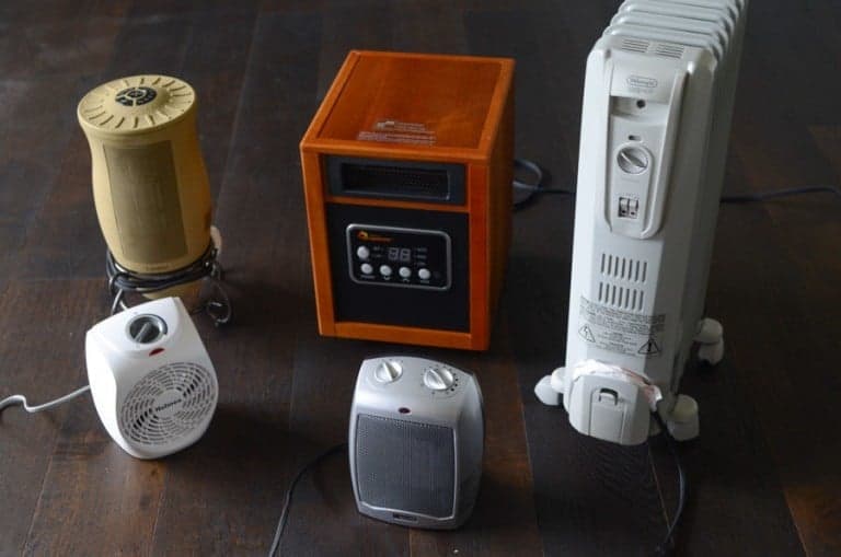 Five different space heaters are arranged on a wooden floor.