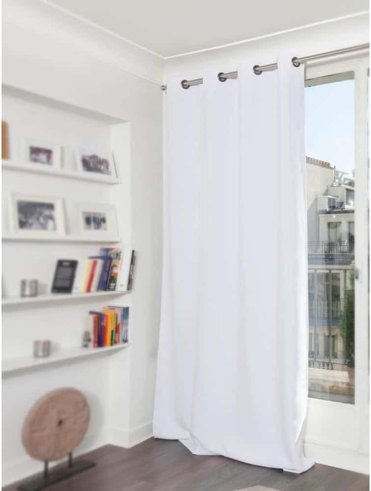 A white curtain hangs on a window with a city view. Adjacent are white shelves with books and framed photos. The room has dark wooden flooring.