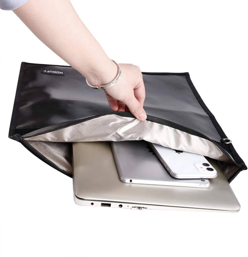 A hand places a laptop, tablet, and smartphone into a black and silver protective case.