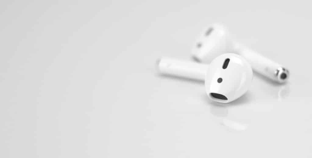 Two white wireless earbuds on a smooth, light gray surface.