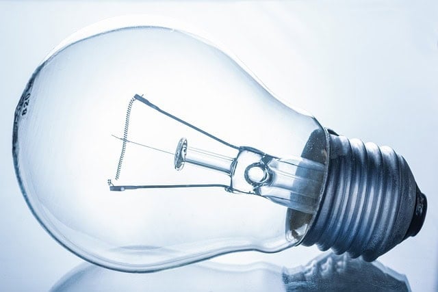A clear incandescent light bulb lies on its side against a light blue background.