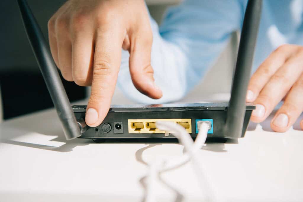 A person presses a button on a Wi-Fi router, which has multiple cables connected to its ports.
