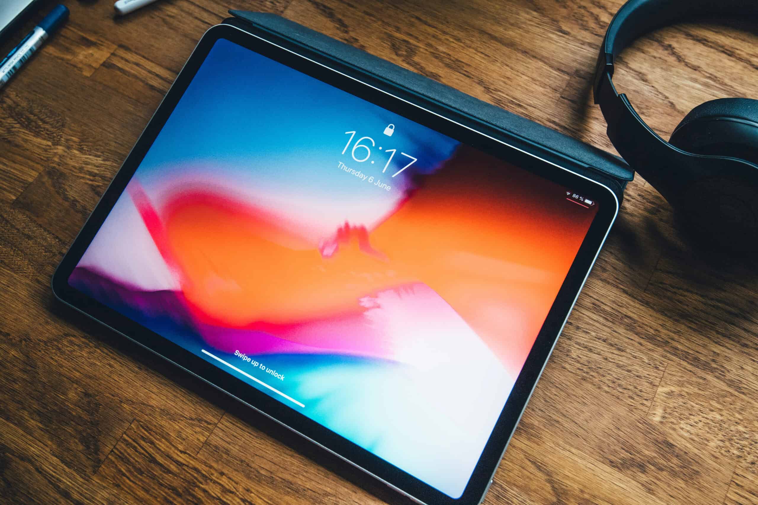 A tablet with a colorful screen displaying the time 16:17 rests on a wooden table next to a pair of black headphones.