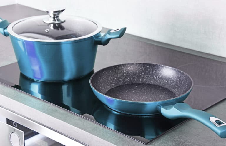 A blue pot with a lid and a blue frying pan sit on a sleek black electric stovetop.