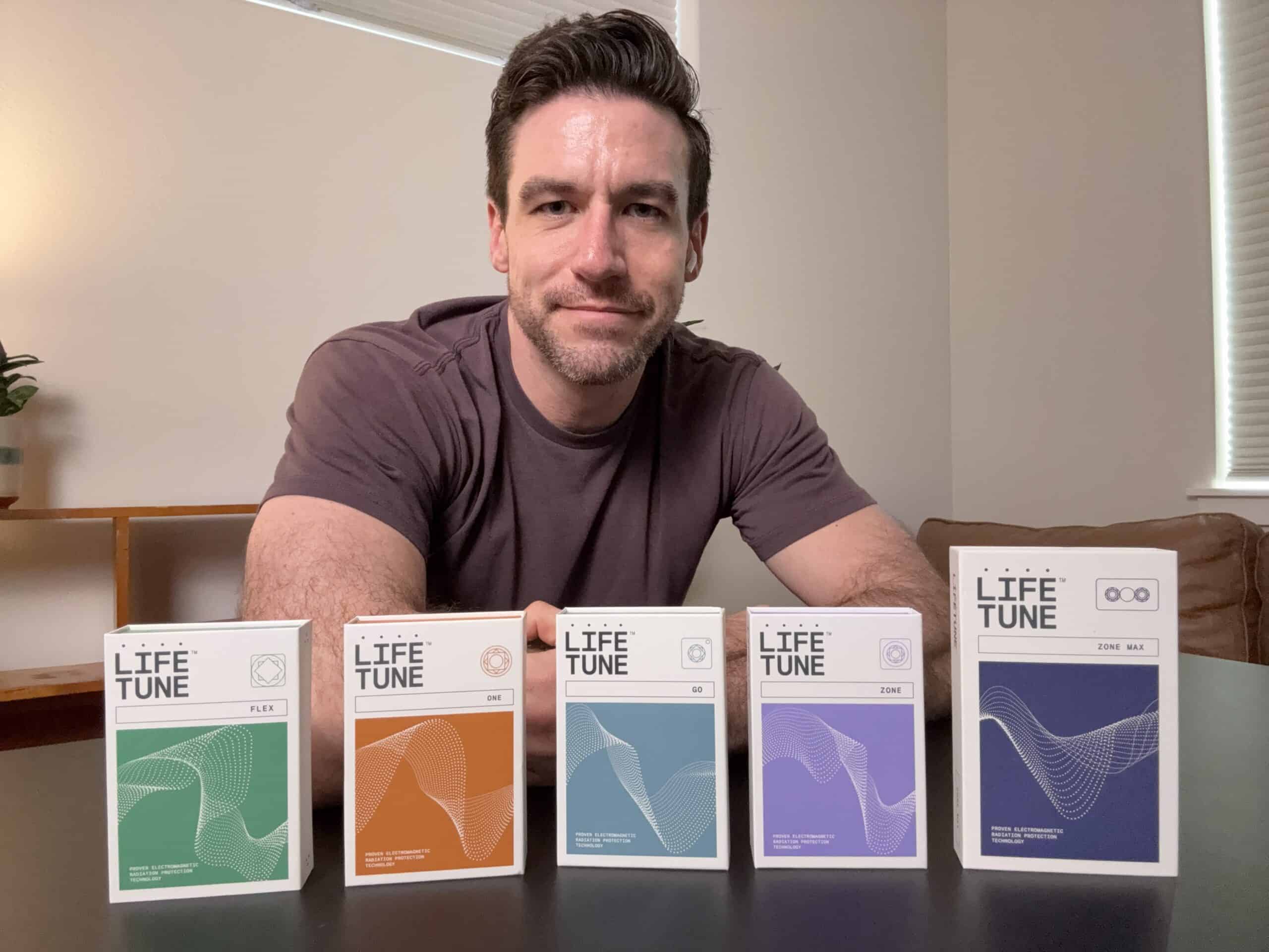 A person sits at a table with five Life Tune product boxes in front of them.