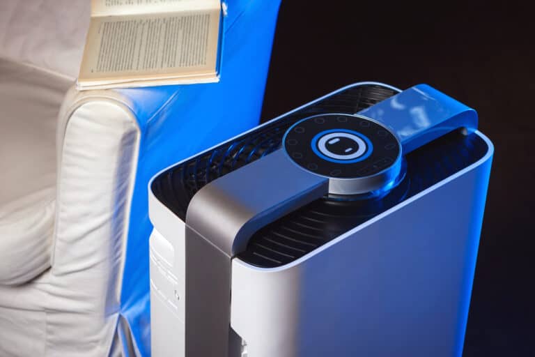 A modern air purifier with digital controls is positioned next to a white armchair. An open book rests on the chairs arm. The scene is lit with blue ambient lighting.
