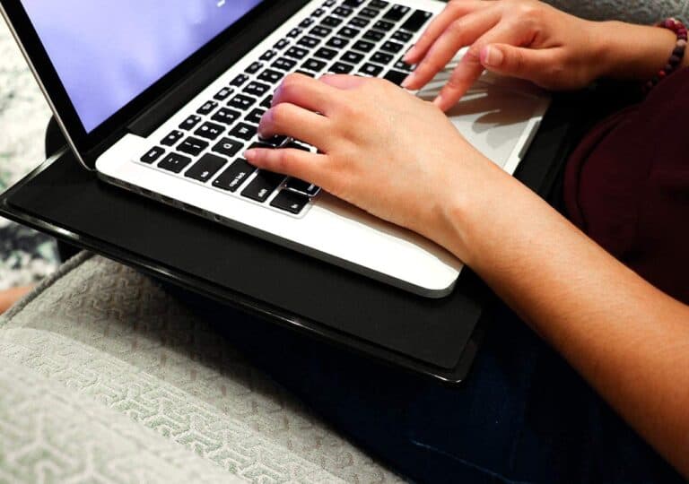 A person typing on a laptop placed on their lap, sitting on a cushioned chair.