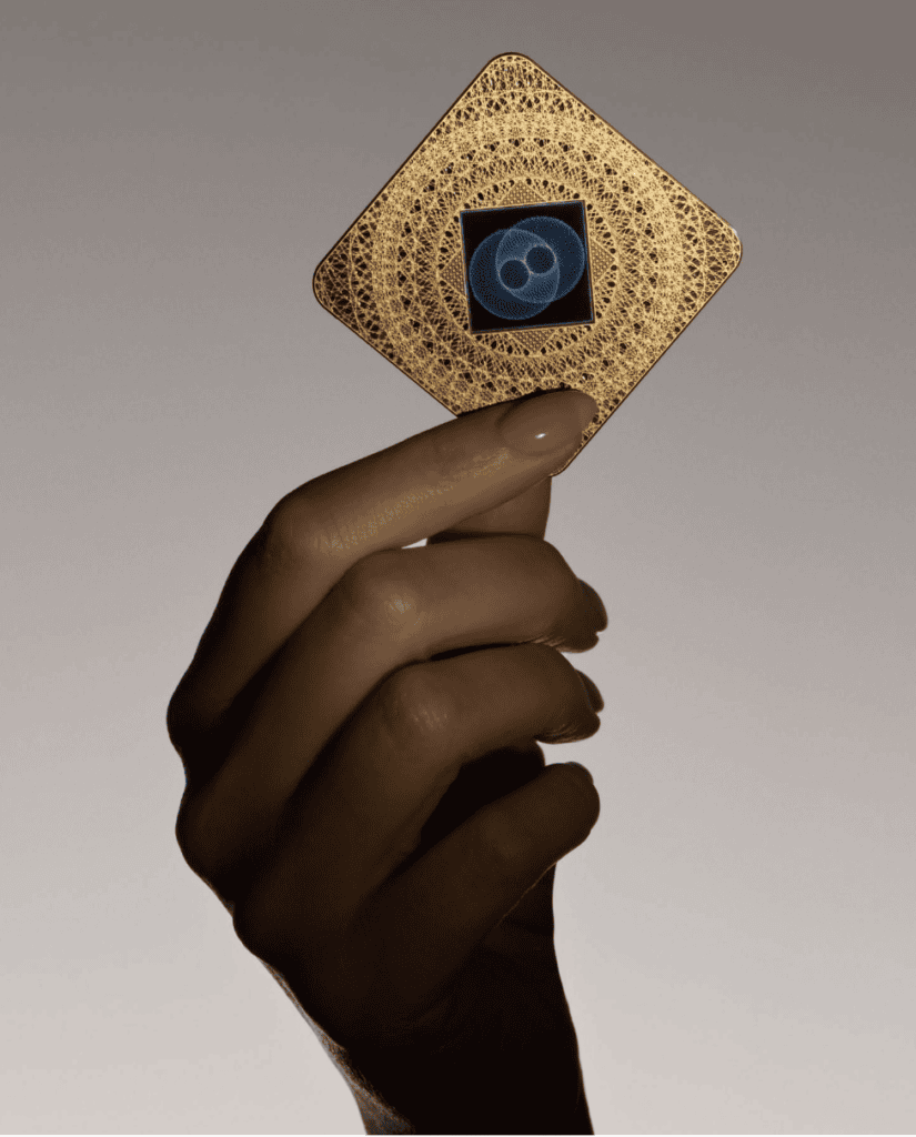 Screenshot 2026-01-06 at 92906 PM - EMF Academy A hand holds a square, gold-colored object with intricate patterns and a black center displaying a blue, circular design.