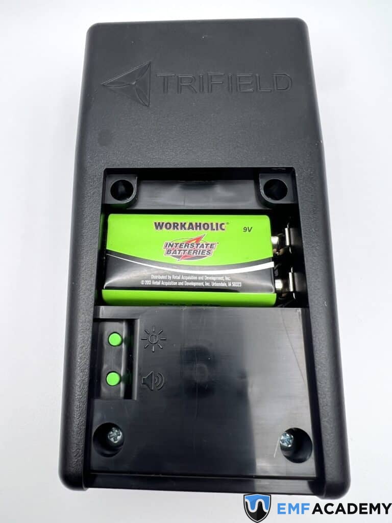 Close-up of a Trifield device with an open battery compartment, showing the screen light and audio buttons.
