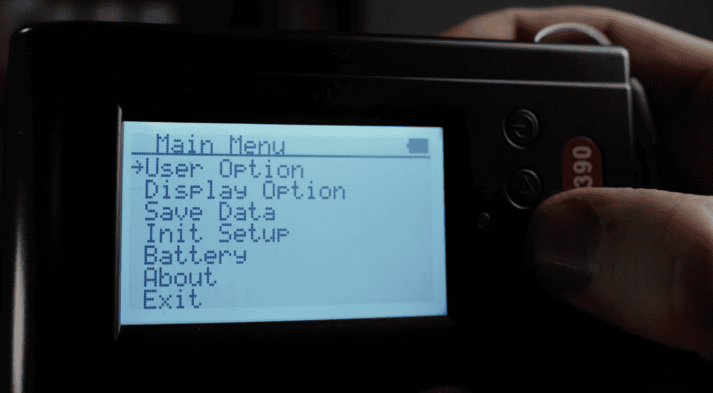Settings and Options - EMF Academy Close-up of a device screen showing a main menu with options like User Option, Display Option, Save Data, Init. Setup, Battery, About, and Exit. A hand is holding the device.