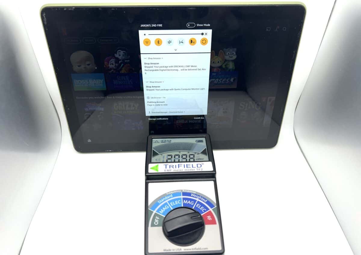 A tablet displaying a screen is behind a TriField meter with its dial set to measure electric and magnetic fields, placed on a white surface.