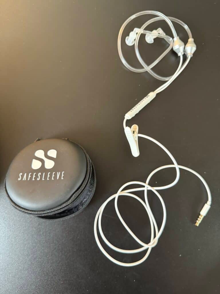 Coiled wired earphones next to a round black Safesleeve case on a dark surface.
