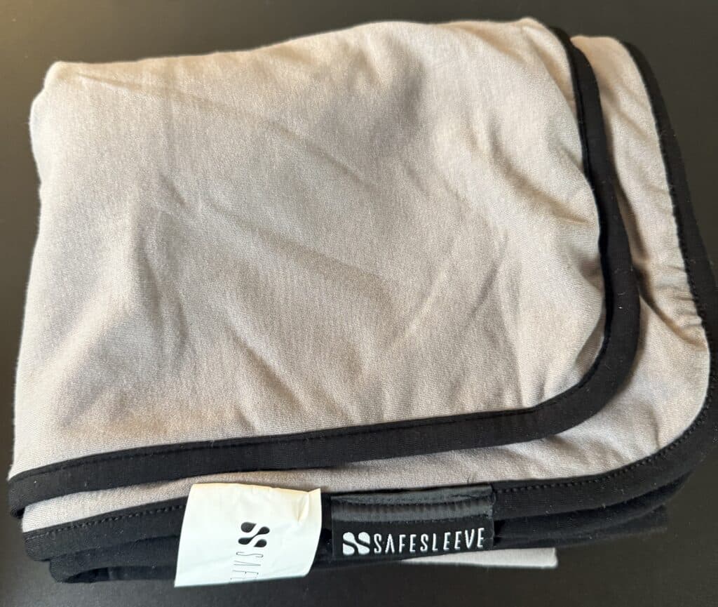 Folded Safesleeve blanket with gray fabric and black trim, featuring a visible brand logo tag.