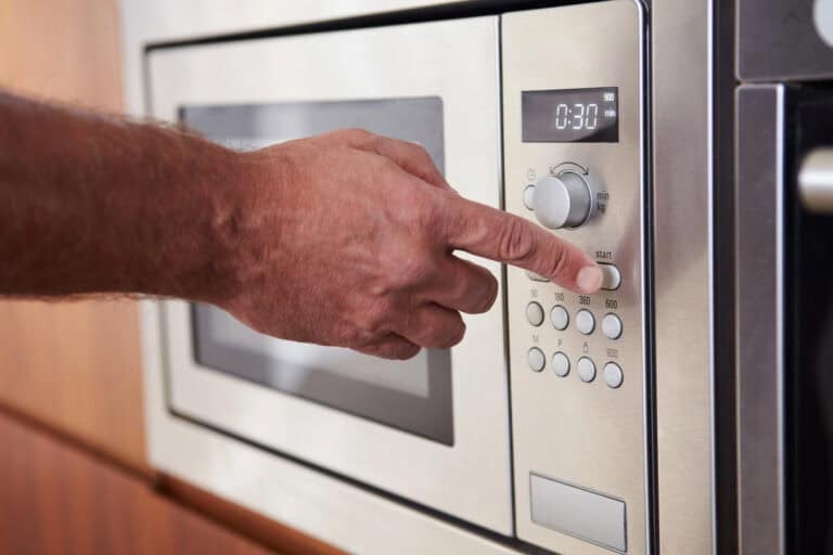 A person sets the timer on a microwave, shown at 30 seconds, using the control panel.