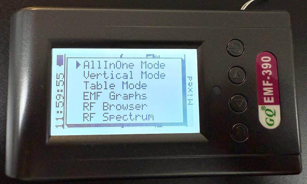 A close-up of a digital EMF-390 meter screen displaying menu options such as AllInOne Mode, Vertical Mode, Table Mode, EMF Graphs, RF Browser, and RF Spectrum.