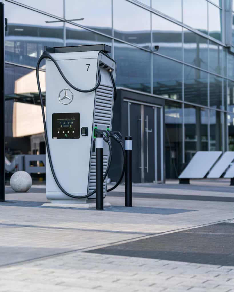 EMF EV - EMF Academy A Mercedes-Benz electric vehicle charging station stands outside a modern glass building, with charging cables and display screen visible.